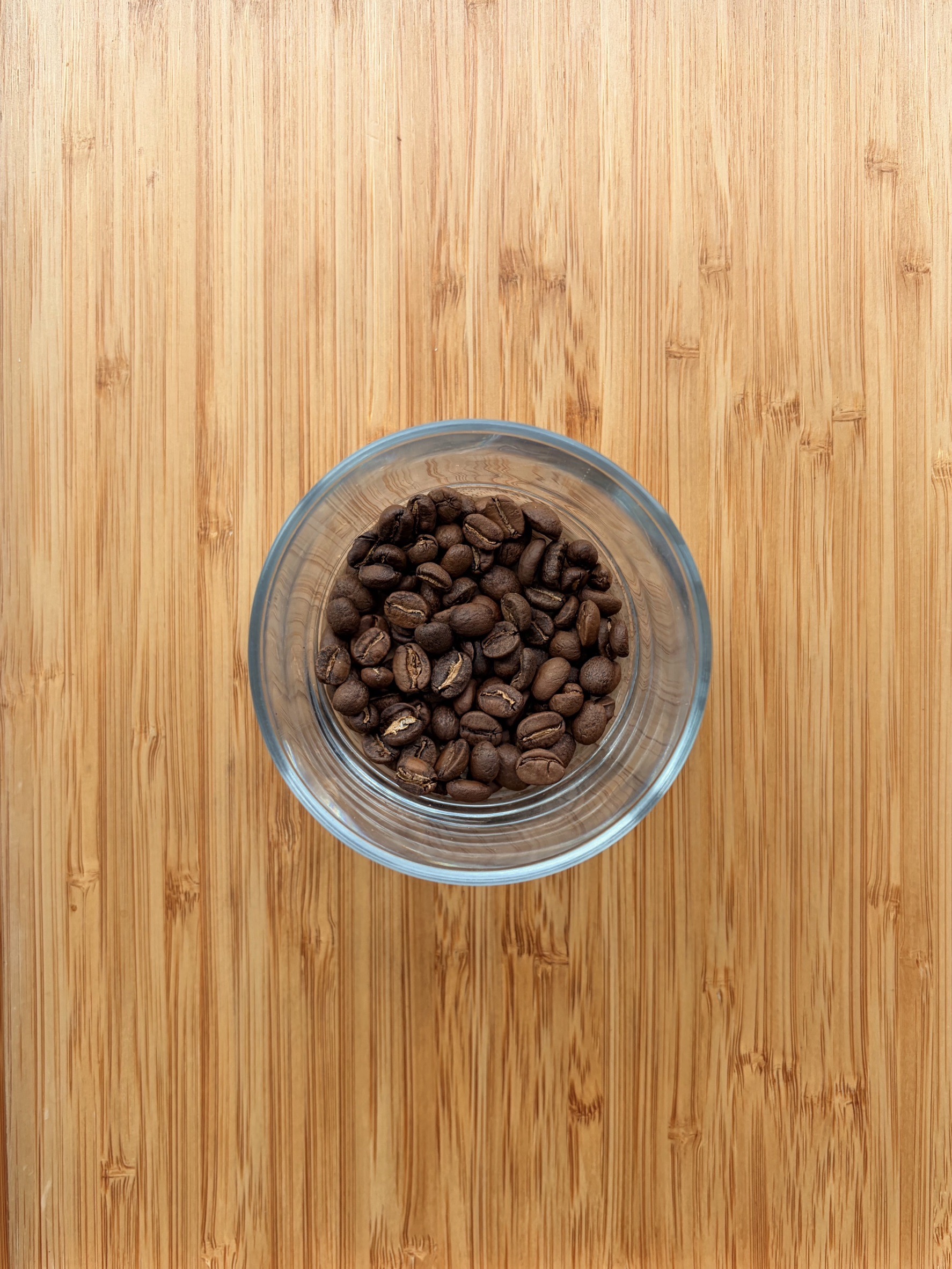 Roasted coffee beans in a glass bowl on bamboo